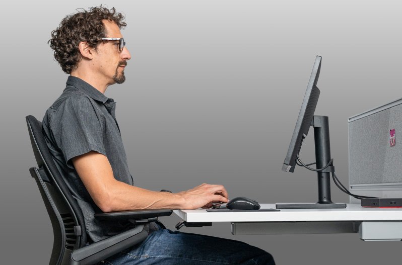 Gute Körperhaltung durch Bildschirmarbeitsbrille: Ein Mann sitzt aufrecht in einem ergonomischen Bürostuhl und blickt entspannt durch eine Bildschirmarbeitsbrille auf den Monitor.