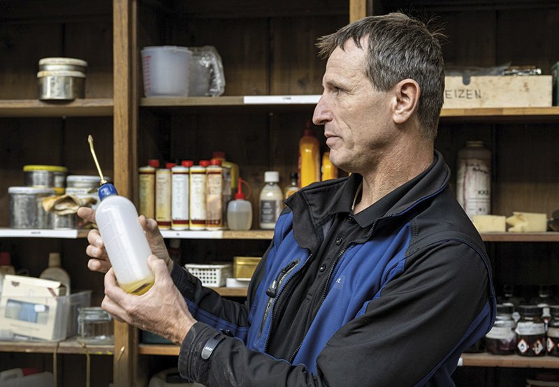 ein Mann hält eine Plastikflasche, dahinter ein Regal mit verschiedenen Gefässen