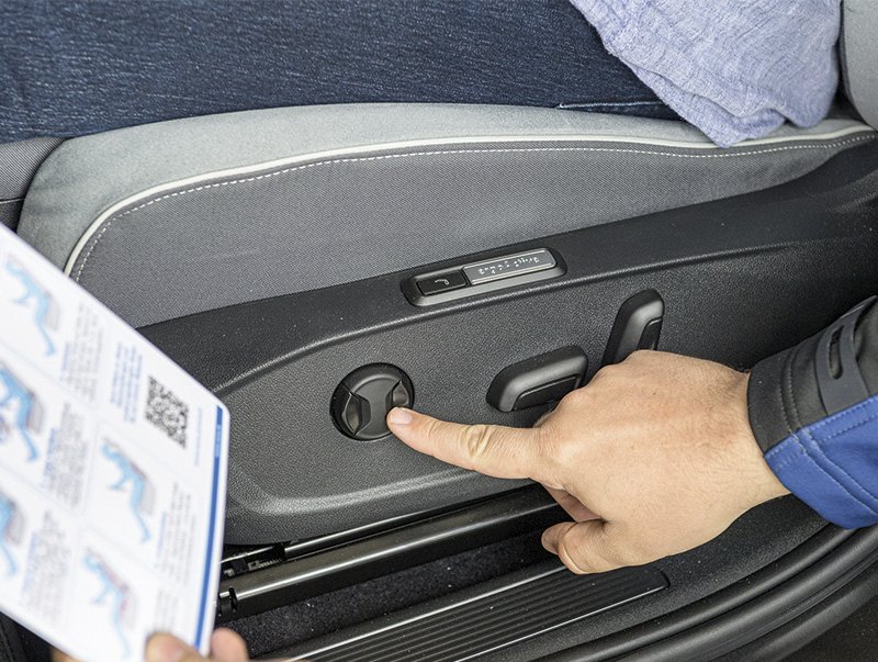 ein Finger drückt auf einen Knopf an der Autotüre, die andere Hand hält eine Anleitung