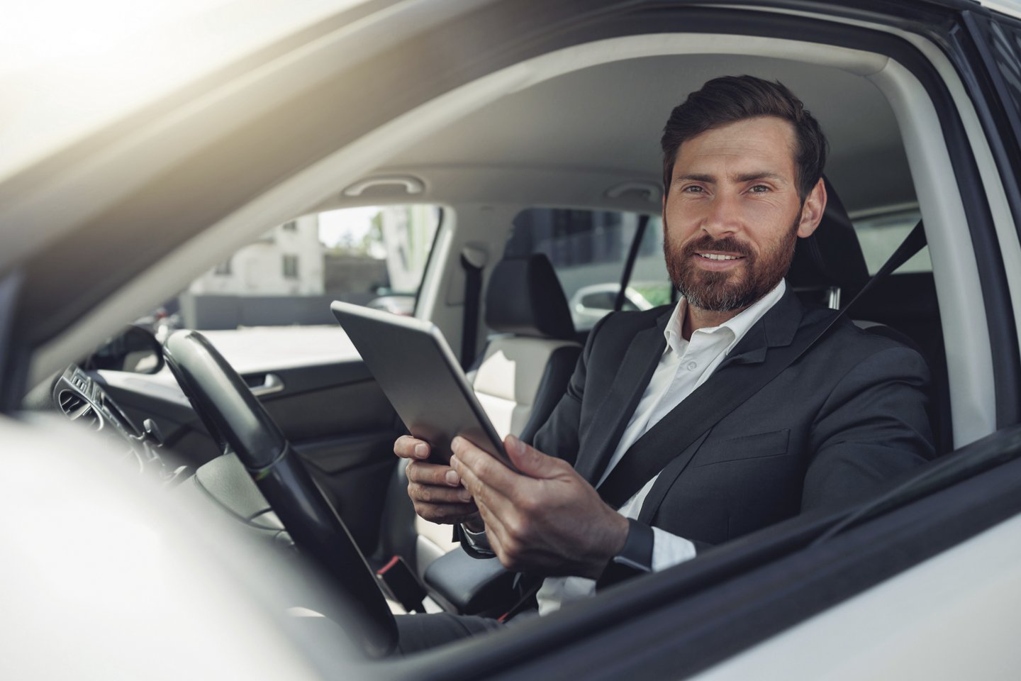 Businessman working on digital tablet while sitting on driver seat in car. Blurred background