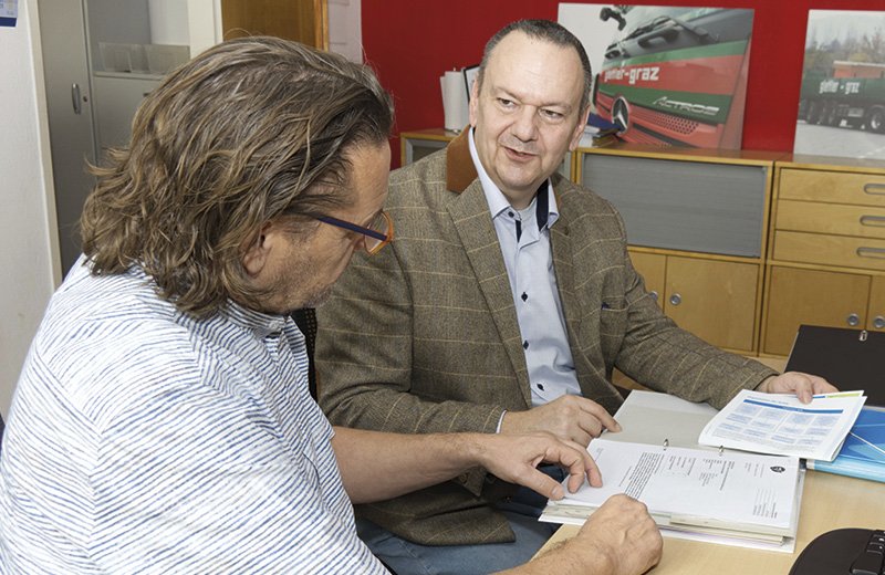 zwei Männer sitzen in einem Büro beieinander und besprechen etwas