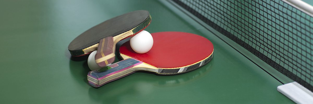 Two table tennis or ping pong rackets and balls on a green table with net